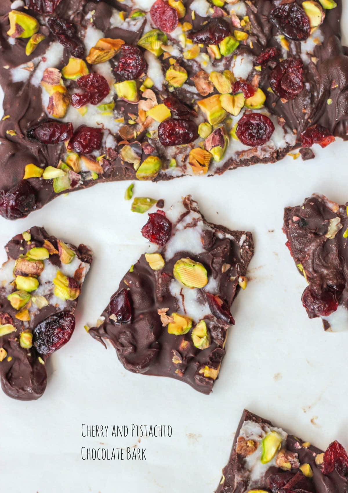 Overhead shot of Cherry Pistachio Chocolate Bark pieces against a white background. There is text in the bottom center of the image that reads "Cherry and Pistachio Chocolate Bark".