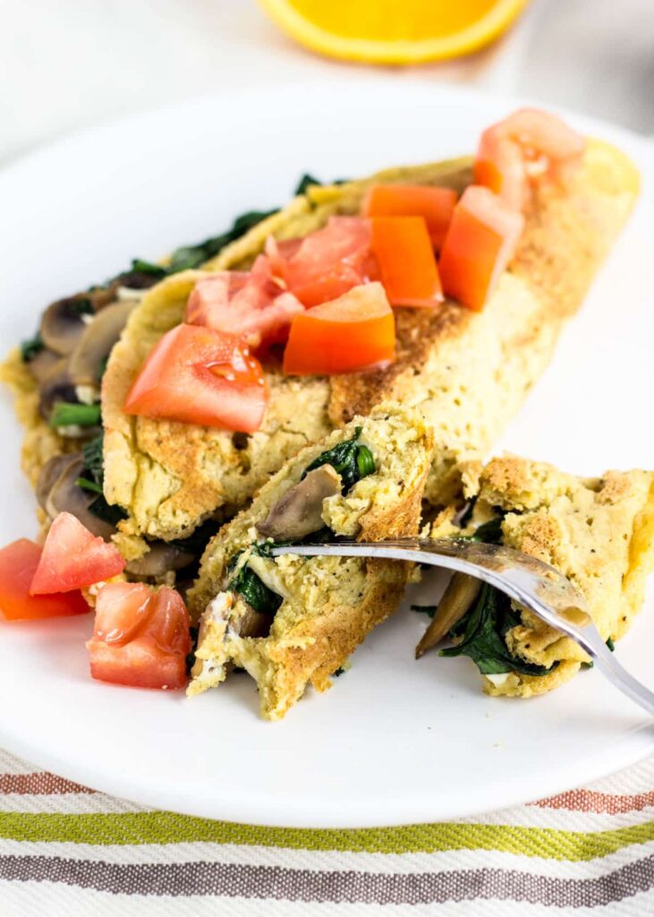 Close up view of Vegan Chickpea Flour Omelette. The omelette is filled with mushrooms, spinach, cheese and topped with fresh tomato.
