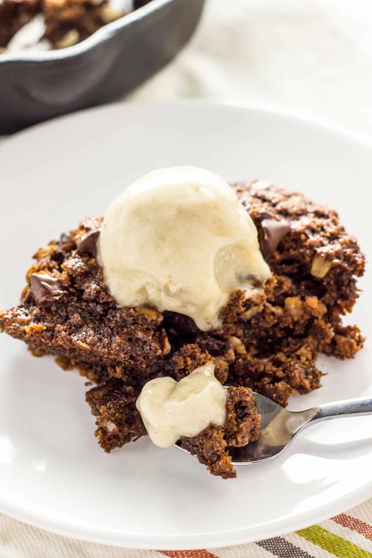 A small plate with a serving of Chocolate Chip Oatmeal Cookie Skillet topped with vegan vanilla ice cream.