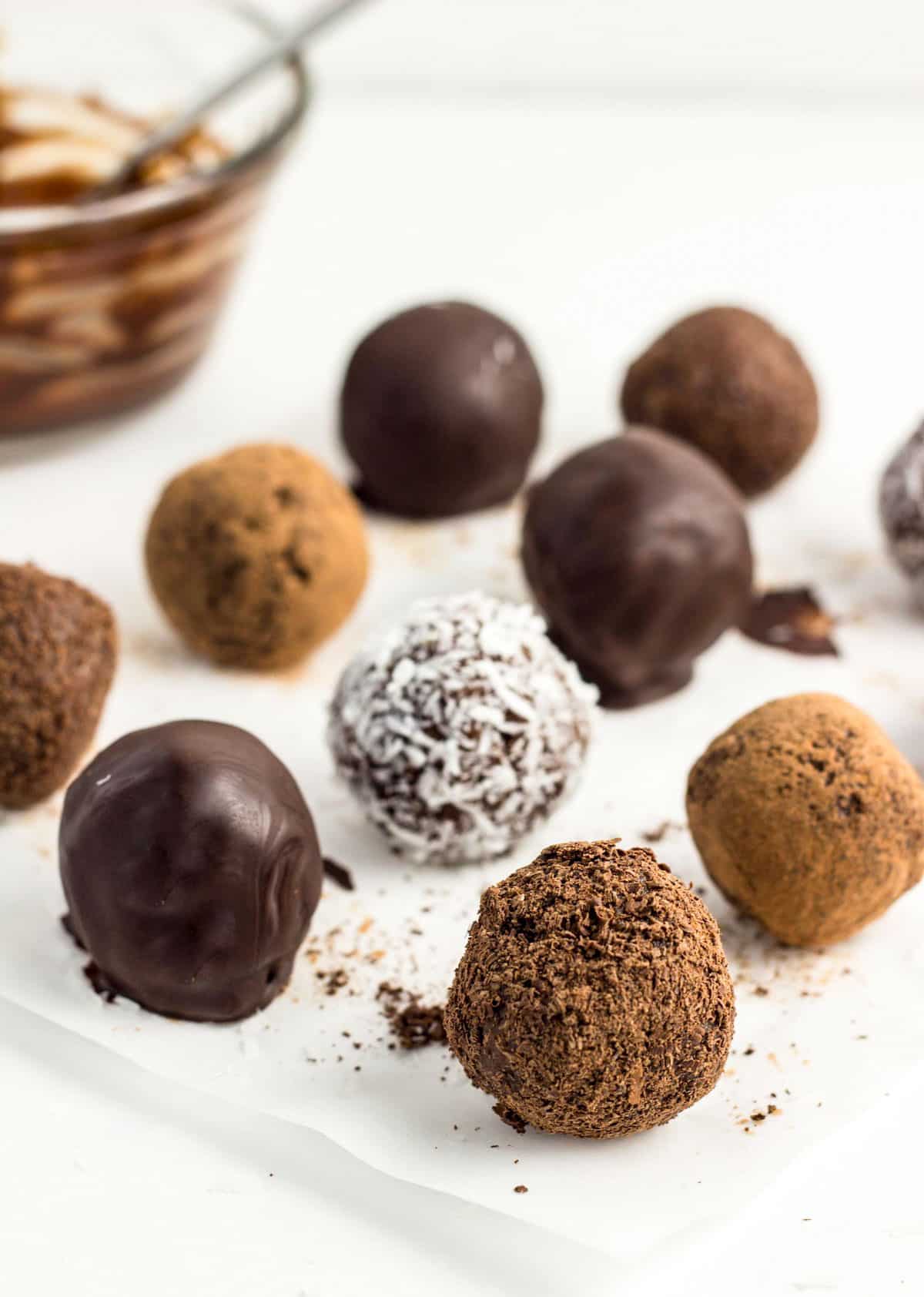 Chocolate Coconut Butter Truffles on parchment paper. There are different exterior coatings including chocolate dipped, cocoa dusted, chocolate shavings, and dried coconut.