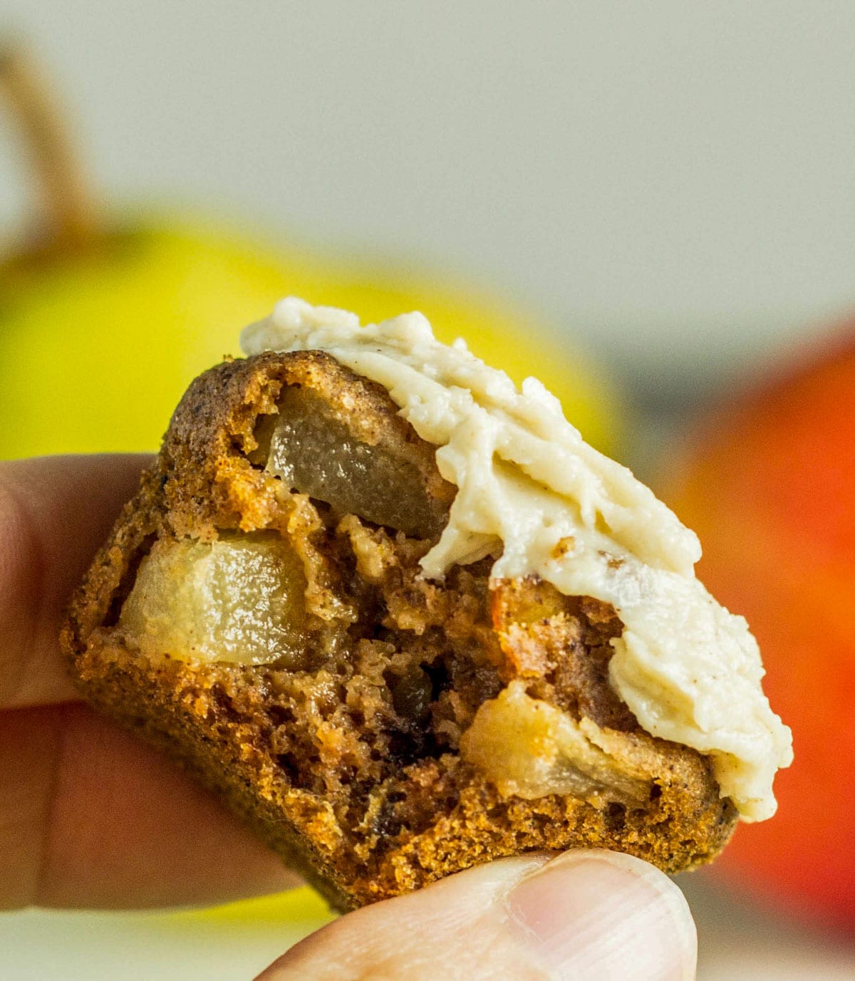 Close up of a hand holding a Cinnamon Pear Mini Muffin. The muffin is cut open to show small chunks of pear in the crumb.
