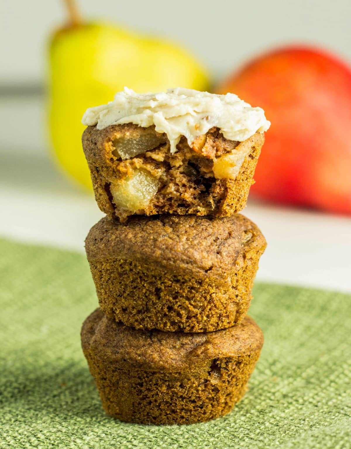 A stack of three Cinnamon Pear Mini Muffins. The top muffin is cut in half to show interior and has a cashew based frosting on top.