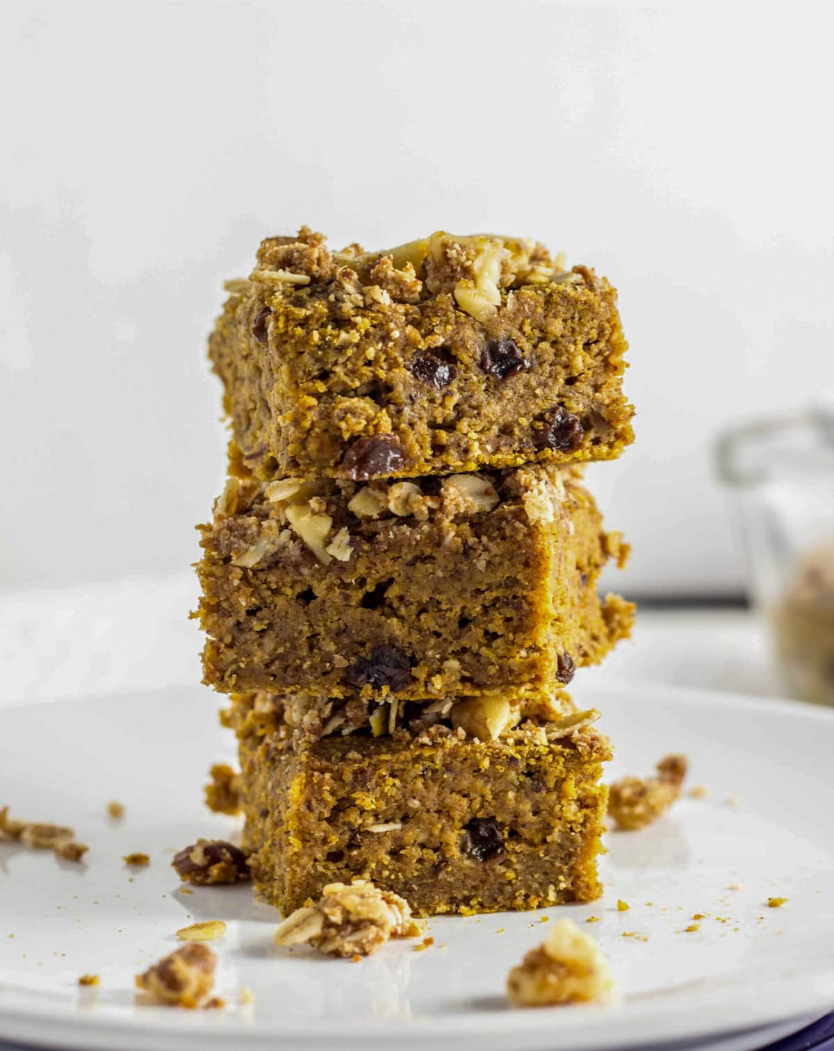 Three Cinnamon Raisin Butternut Squash Squares stacked up on a small white plate. There is loose streusel topping on the plate around the stack.