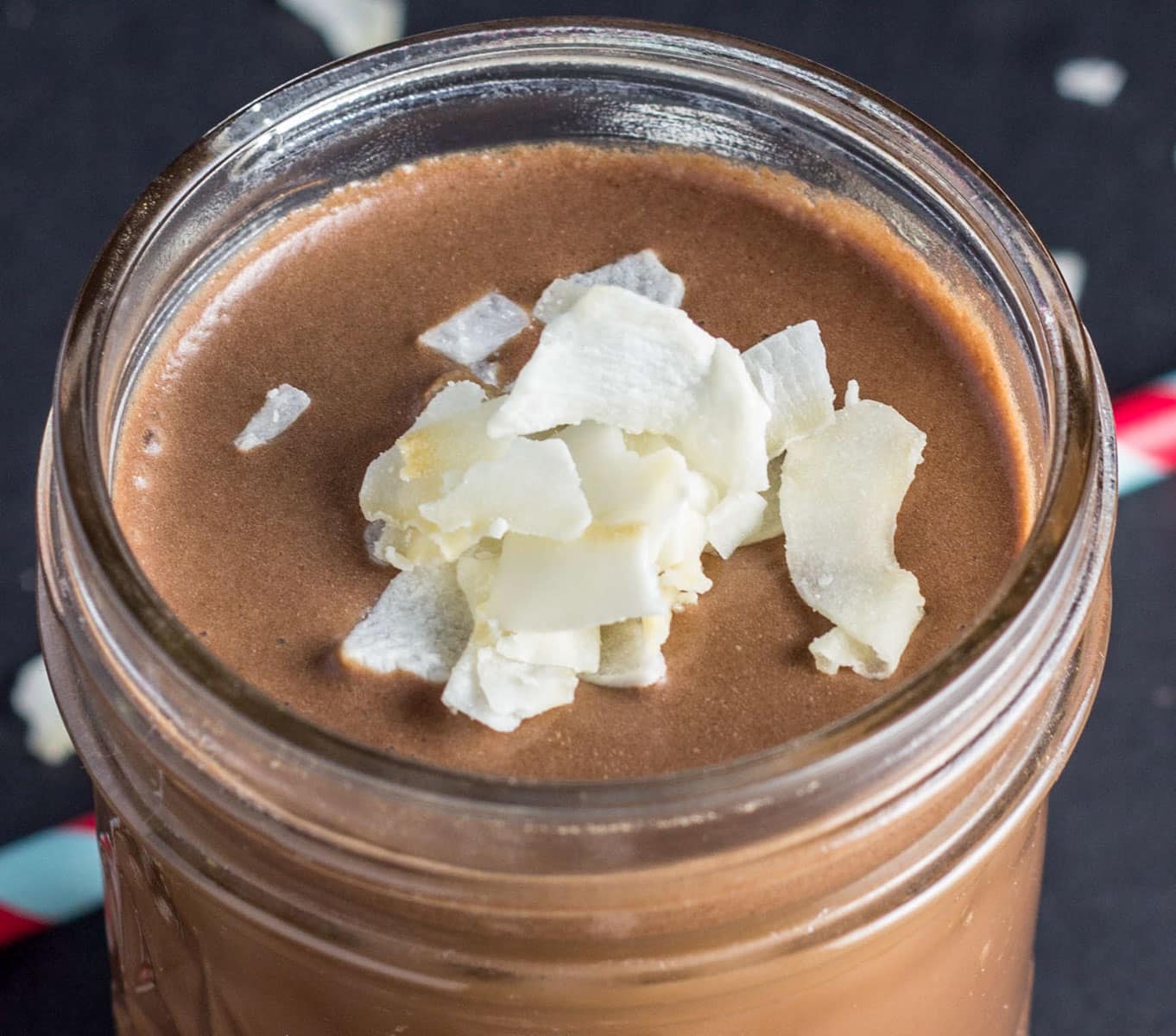 Close up view of a glass with Copycat Chocolate Coconut Water. There are coconut chips on the top of the drink.