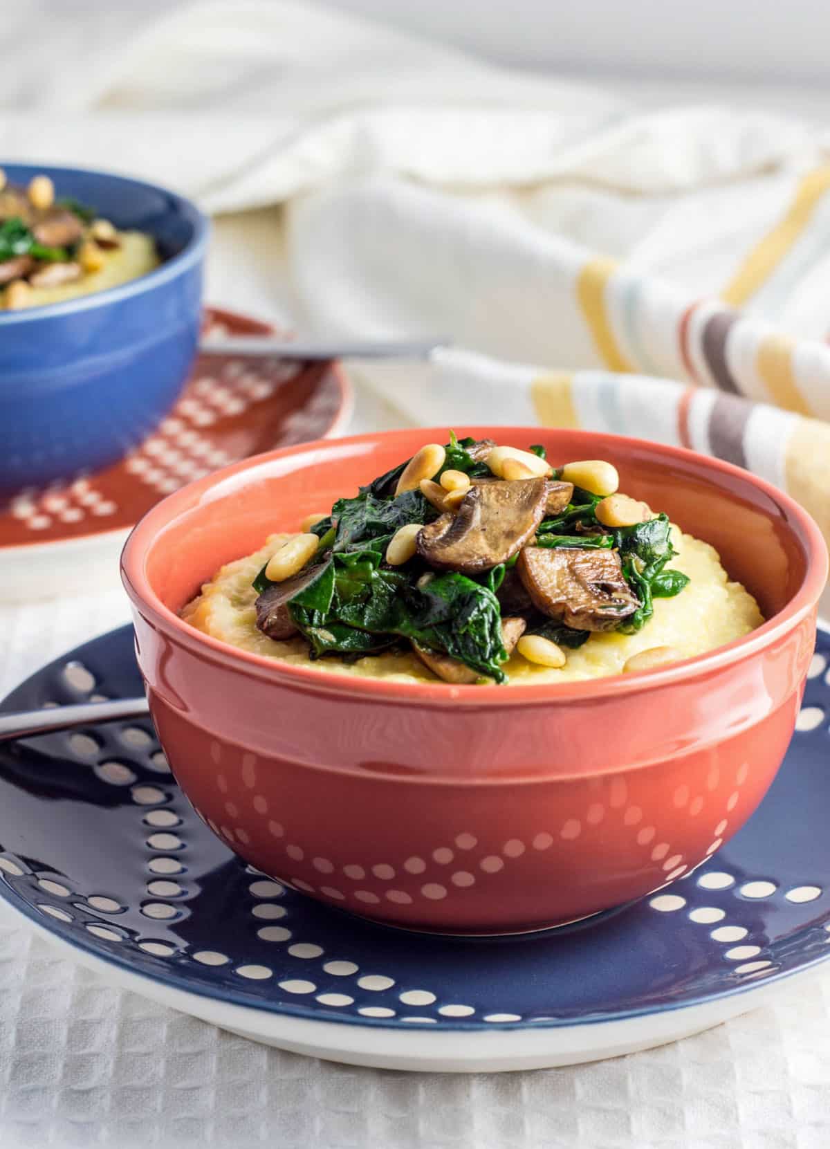 A bowl of Creamy Polenta with Mushrooms and Spinach is in the foreground. In the background is the partial view of a second bowl.