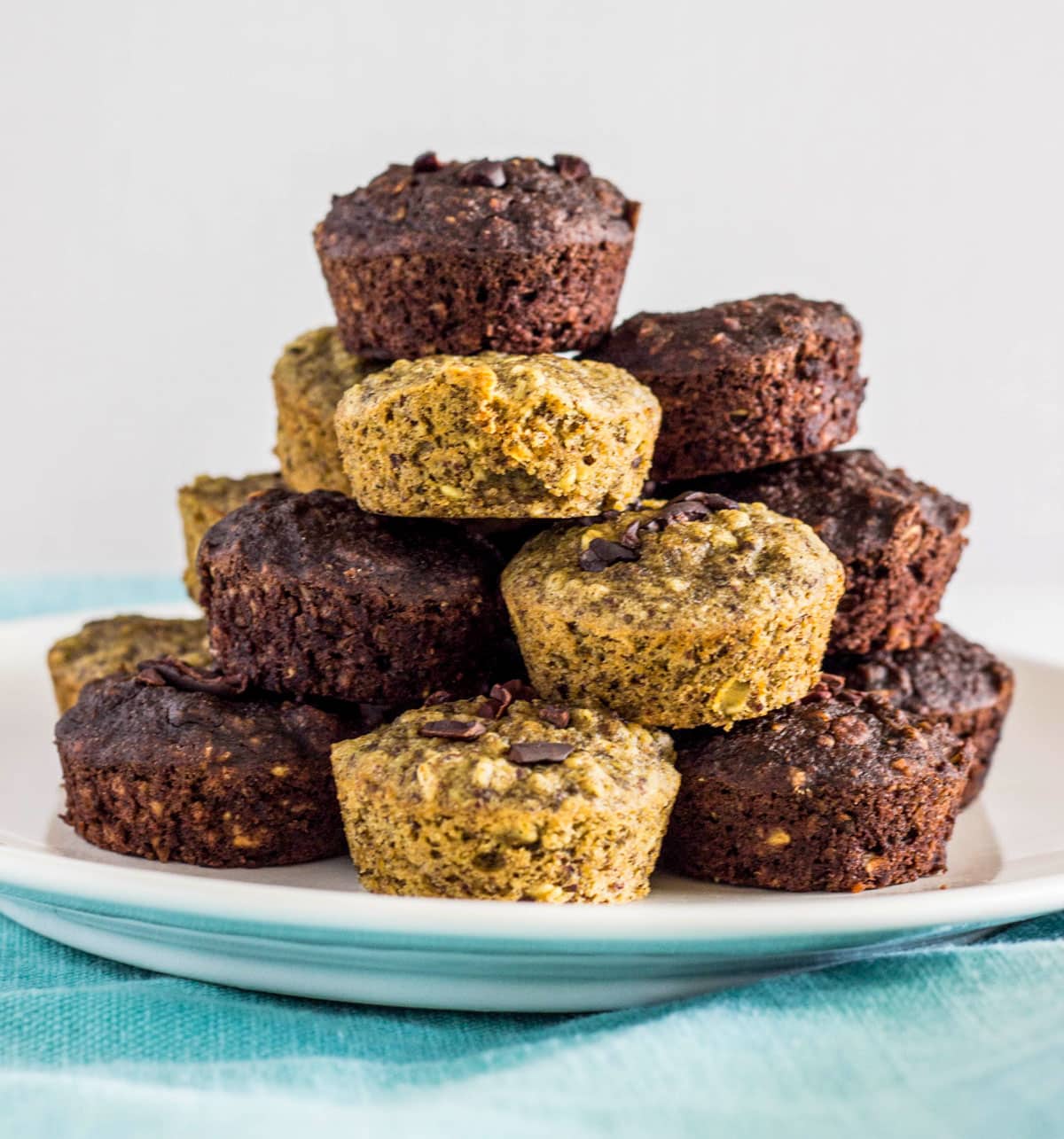 A large stack of Gluten free Oil Free Mini Banana Muffins. Some of the muffins are plain banana bread and some are chocolate banana bread.
