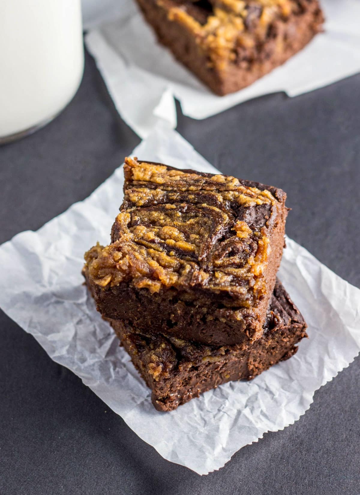 Close up view of two Healthy Peanut Butter Swirl Brownies stacked on a piece of parchment paper.