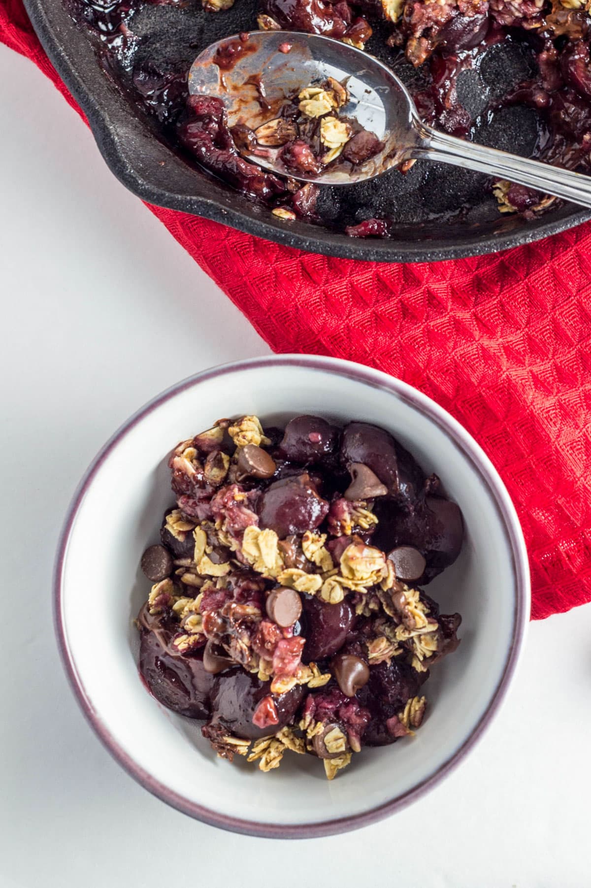 Overhead shot of Vegan Chocolate Cherry Crisp in a small bowl. A cast iron skillet is partially visible in the top of the frame.