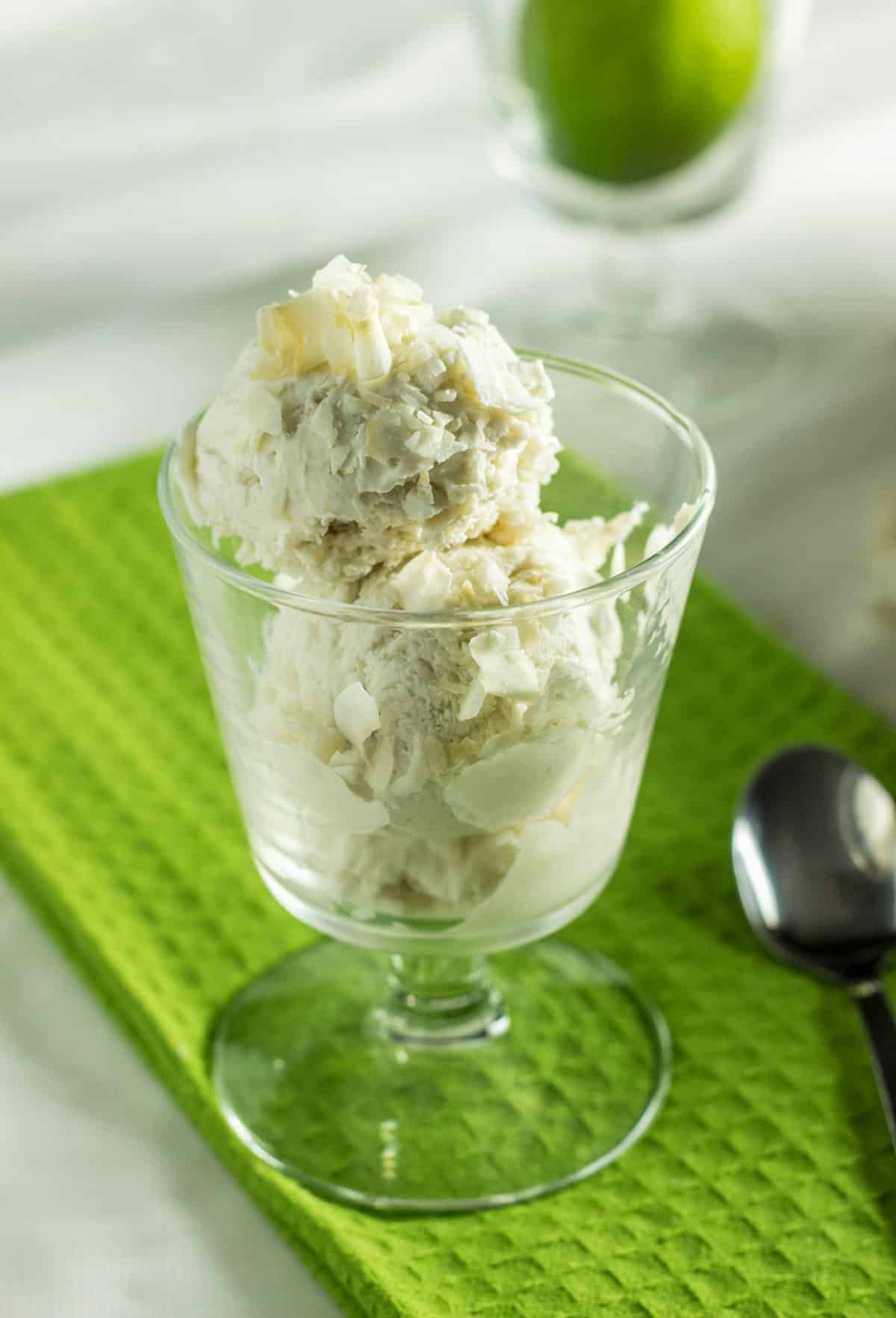 A glass serving cup filled with scoops Vegan coconut Lime Ice Cream. There are coconut chips on top of the ice cream.