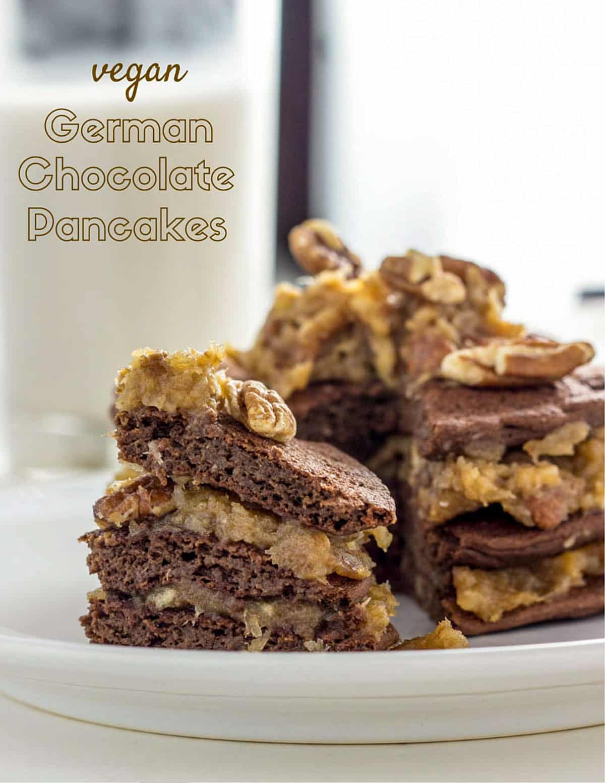 Close up of a stack of Vegan German Chocolate Pancakes on a small white plate. There is text in the upper left corner.