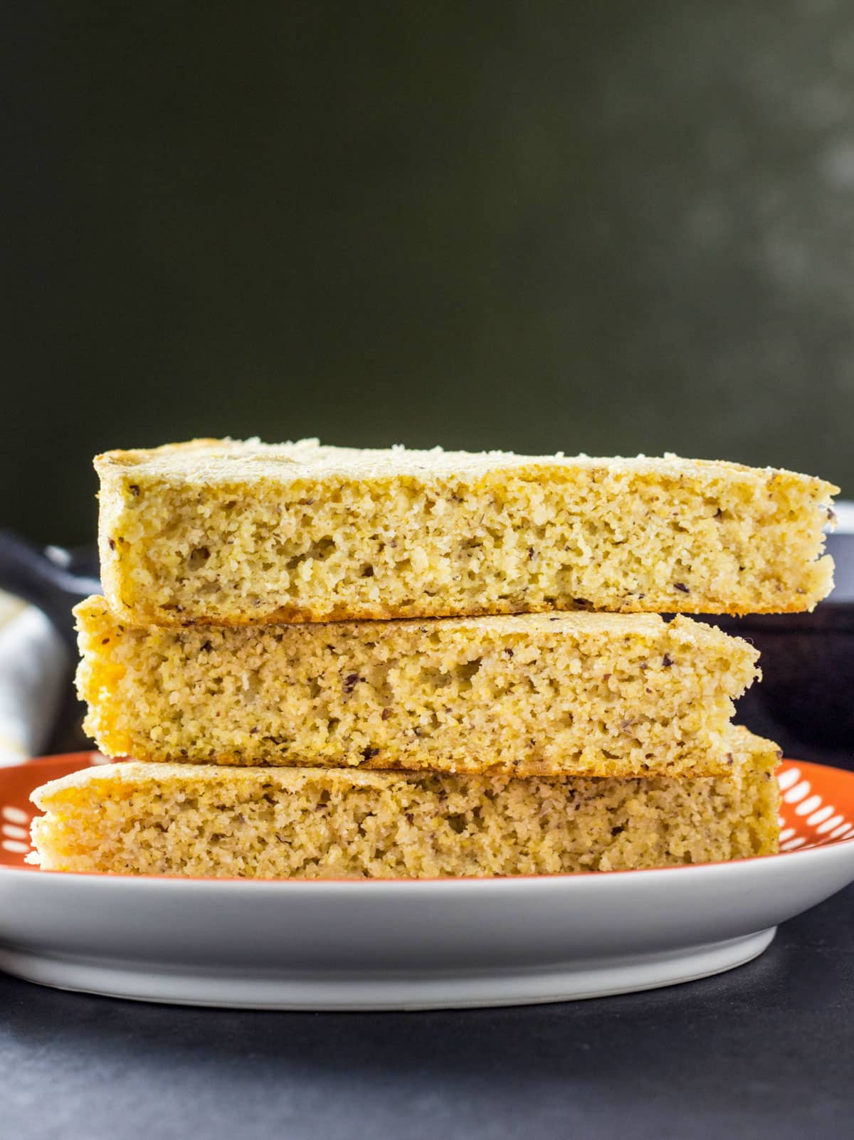 Close up side view of three slices of Vegan Skillet Cornbread stacked on a small plate.
