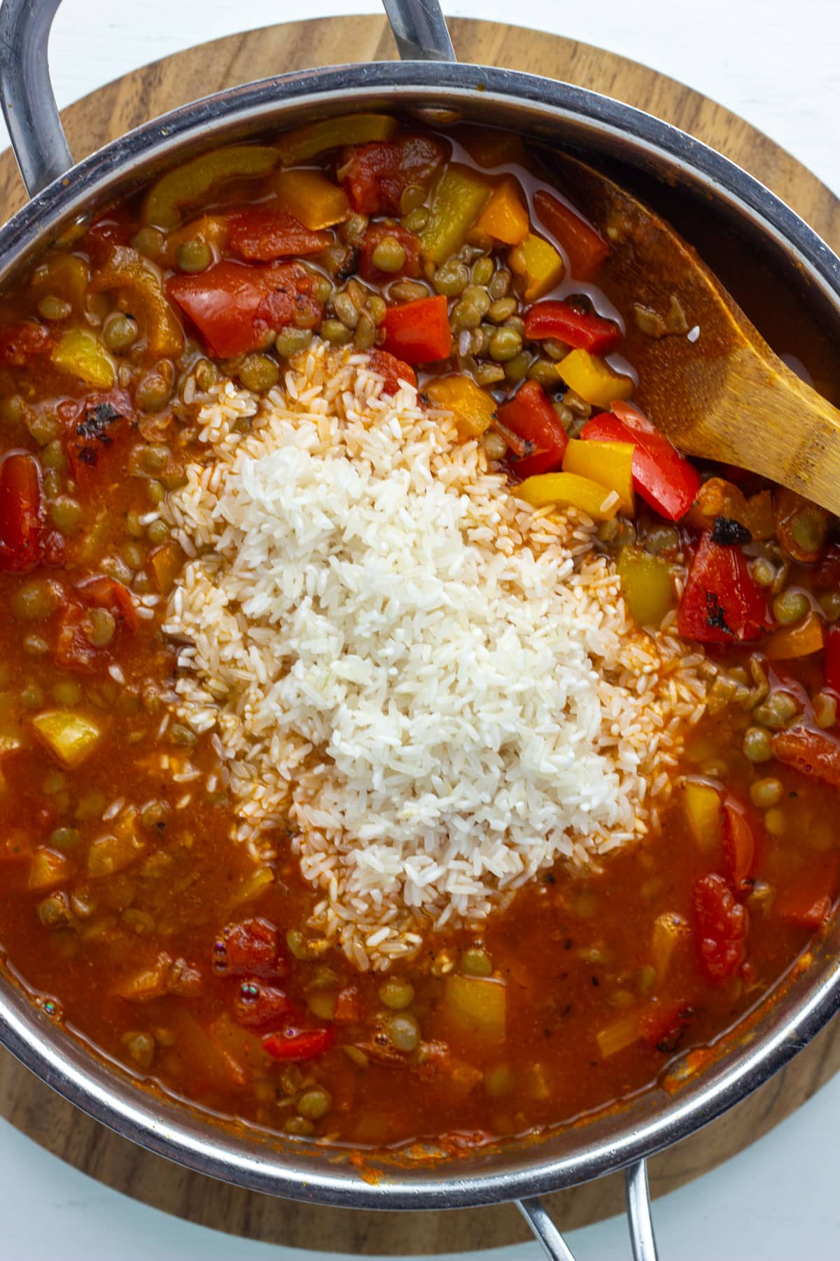 Overhead close up of a skillet with peppers, lentil tomatoes with uncooked rice in the middle.