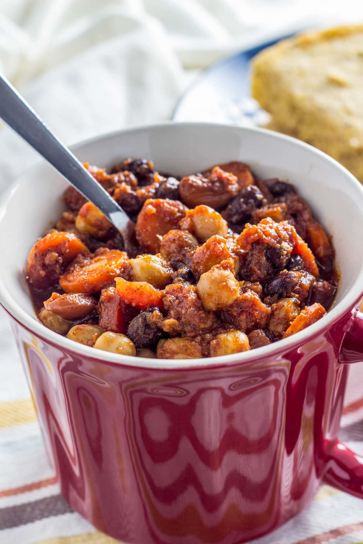 Close up of Vegan Three Bean Chili in a red soup mug. There is a spoon sticking out of the chili.