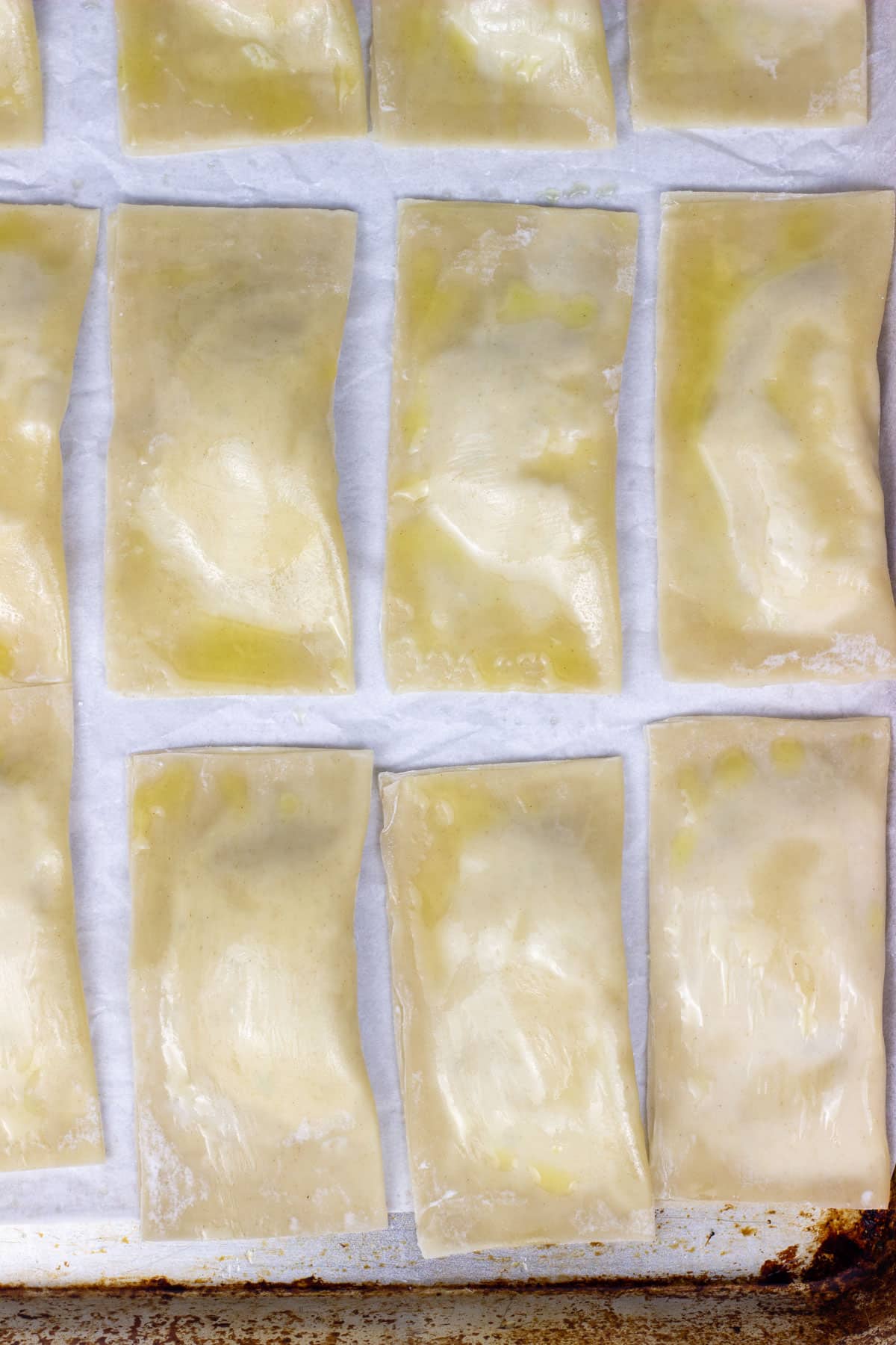 Overhead shot of Wonton Raviolis on a sheet pan before baking. The raviolis have been brushed with oil.