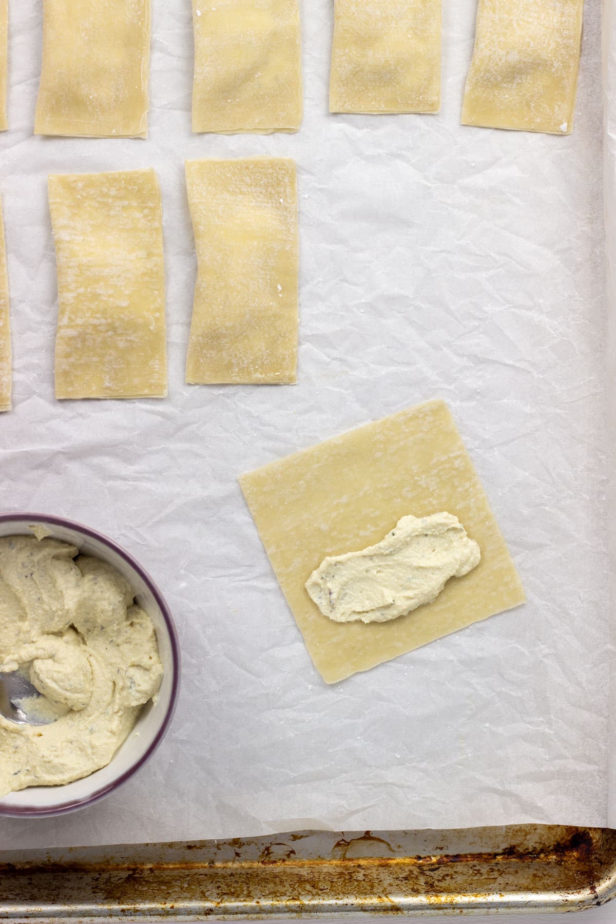 Overhead shot of a wonton wrapper with a small amount of tofu ricotta in the center. There is a bowl of filling to the side and additional filled wrappers in the frame.