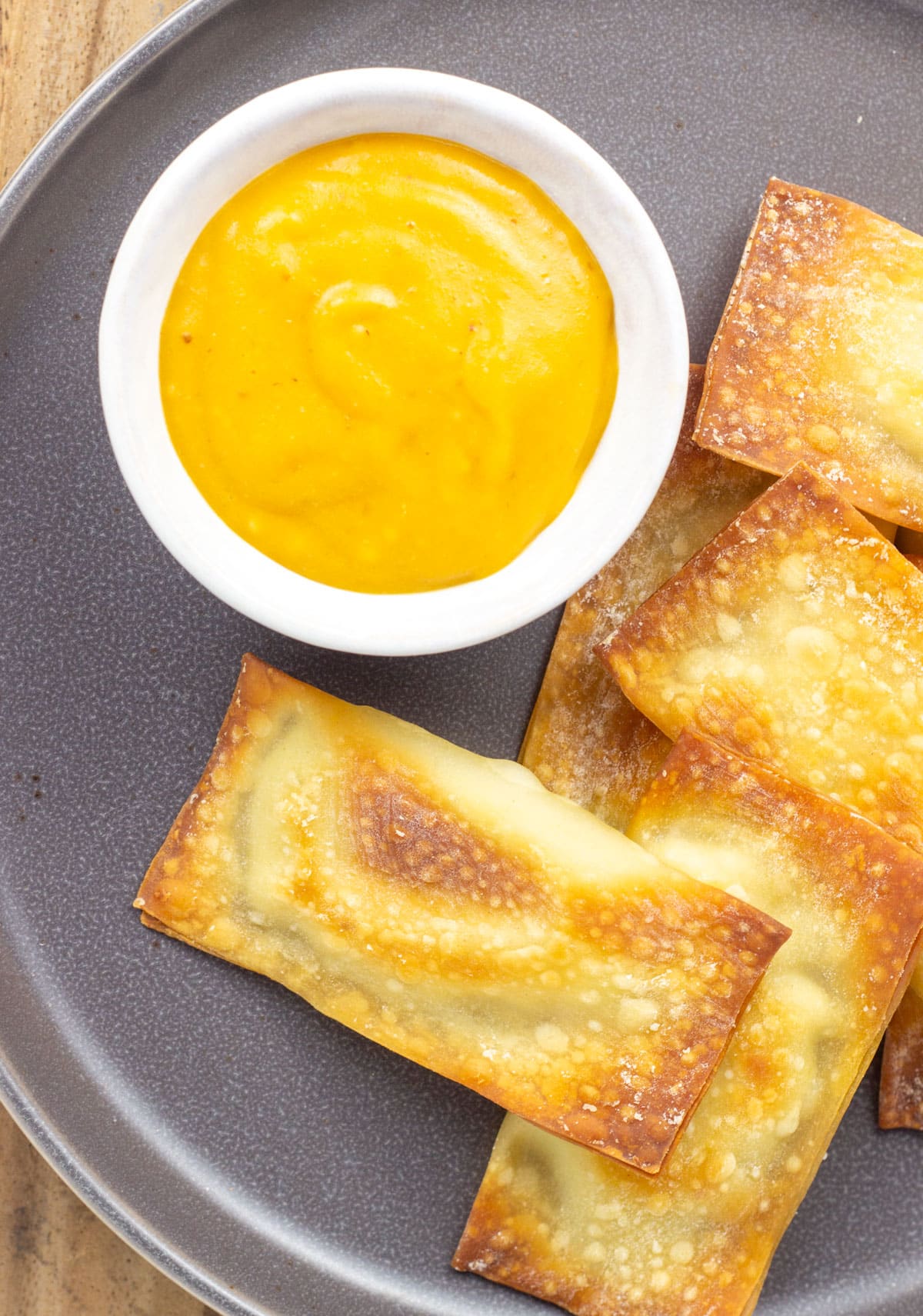 Overhead close up shot of Wonton Ravioli with Pumpkin Cheese Sauce on a small gray plate. The cheese sauce is in a small white bowl.