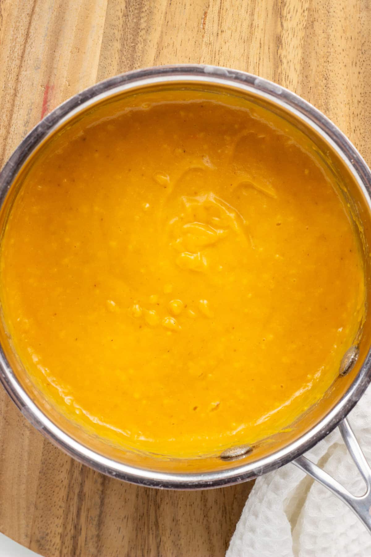 Overhead close up shot of pumpkin cheese in a small sauce pan sitting on a wood board.