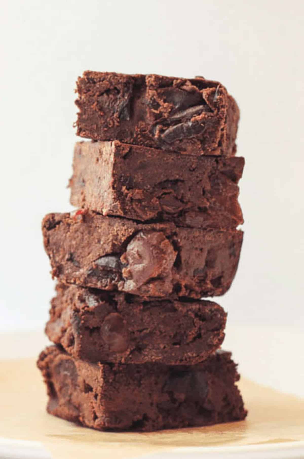 A stack of five Cherry Chocolate Chip Brownies on a piece of tan parchment paper.