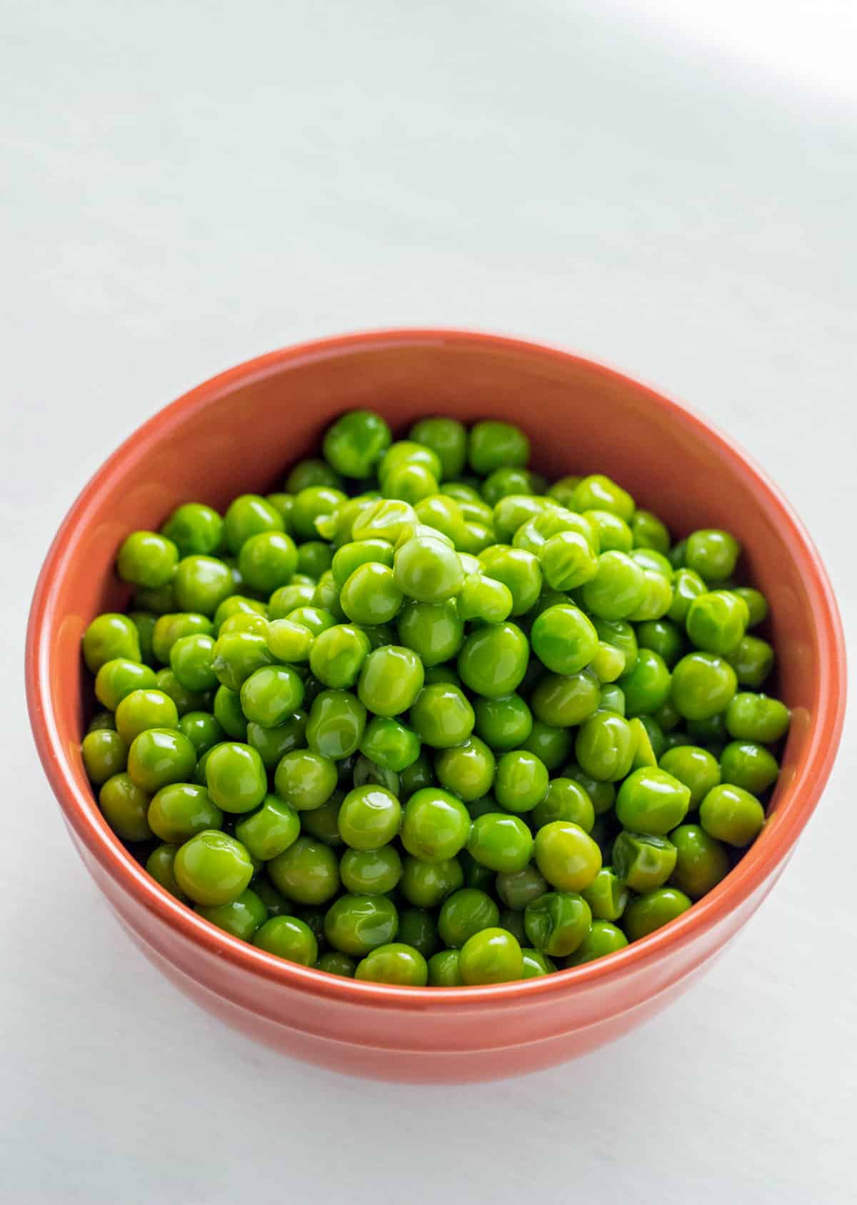 A small orange bowl of peas. An ingredient needed to make Green Pea Hummus.