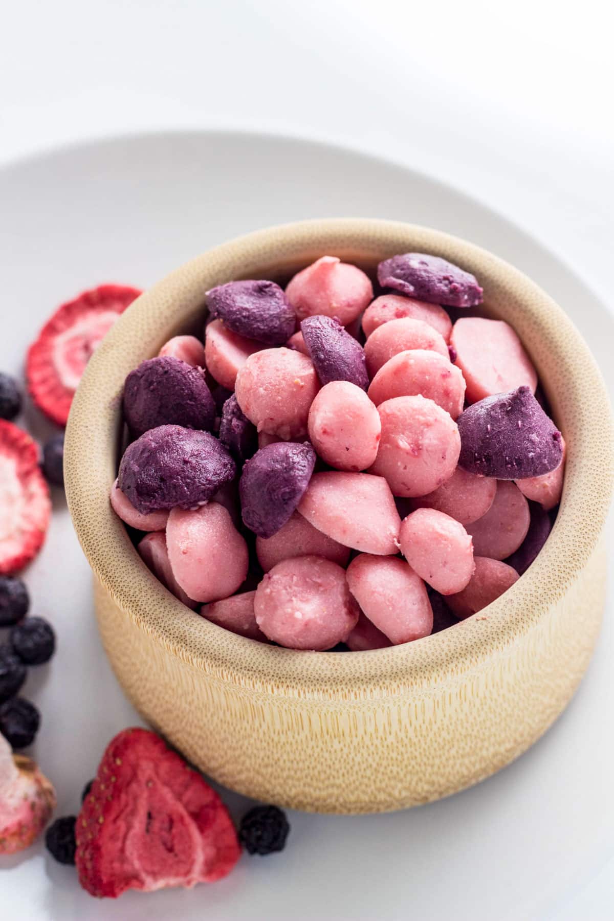 A small wooden bowl of pink and purple Vegan Yogurt Melts for baby. The flavors are strawberry and blueberry.