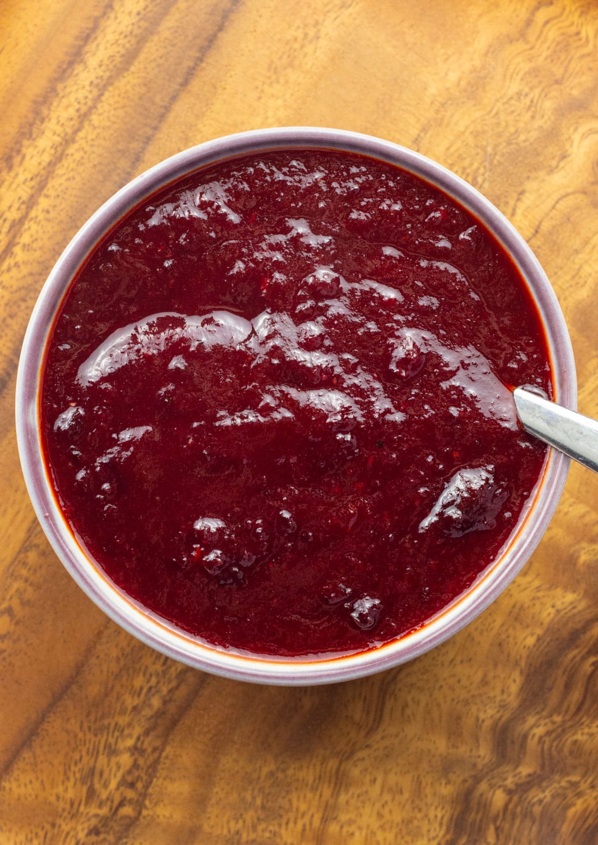 Overhead view of a bowl of Cherry Barbecue Sauce on a wooden board. There is a spoon in the bowl.
