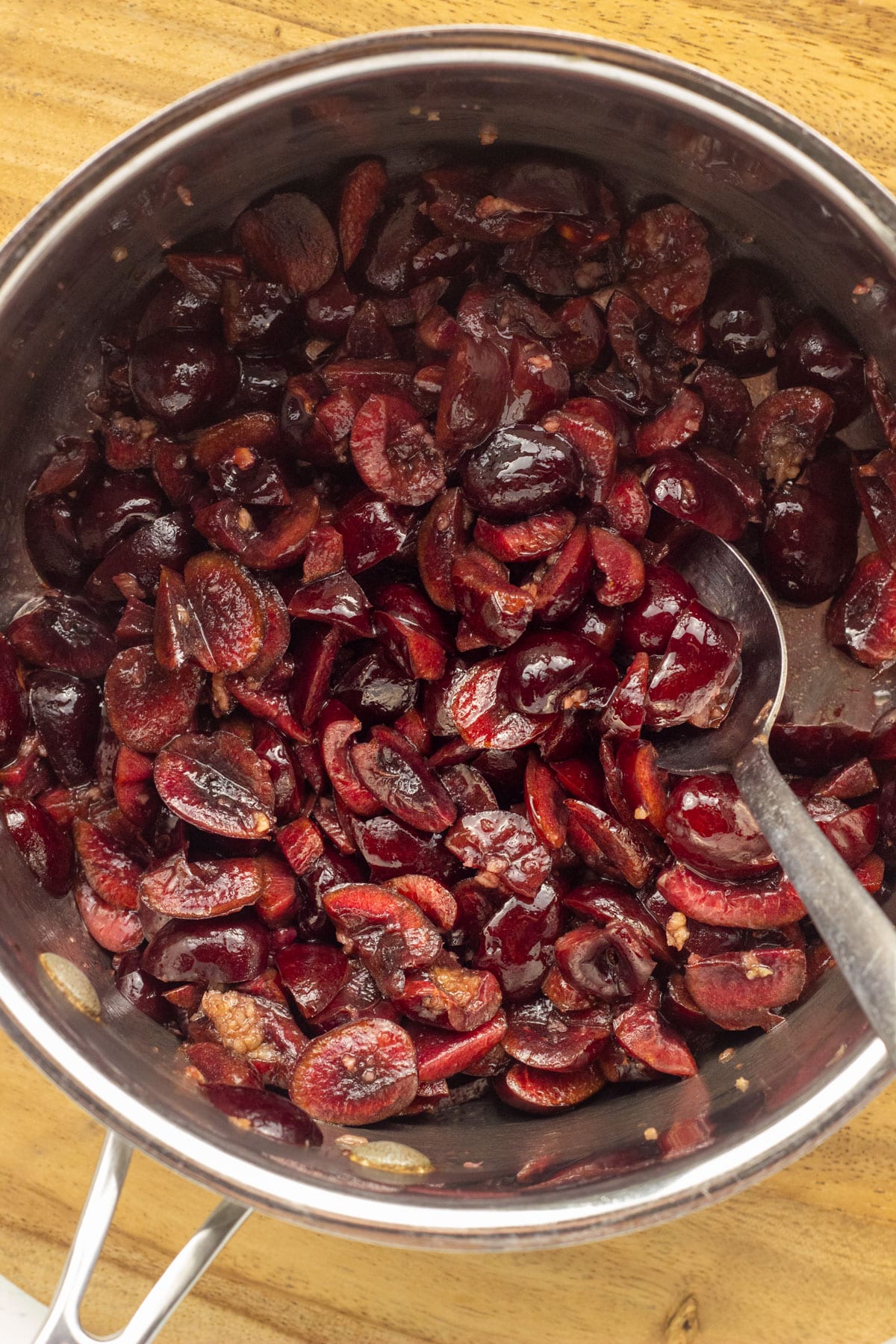Close up of a pot with chopped cherries and garlic. There is a spoon in the pot.