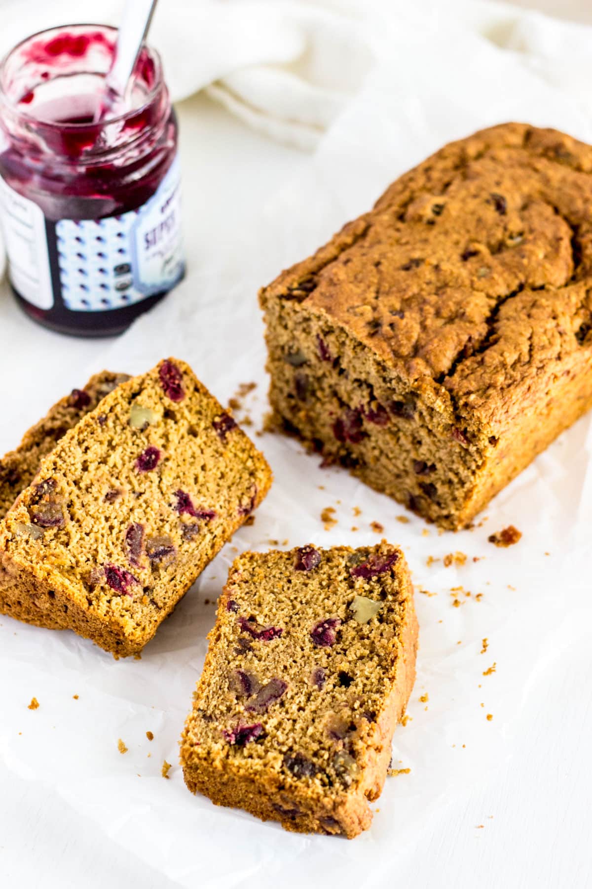 Three slices of Fruit & Nut Breakfast Quick Bread. The remaining loaf and a jar of jam are in the background.