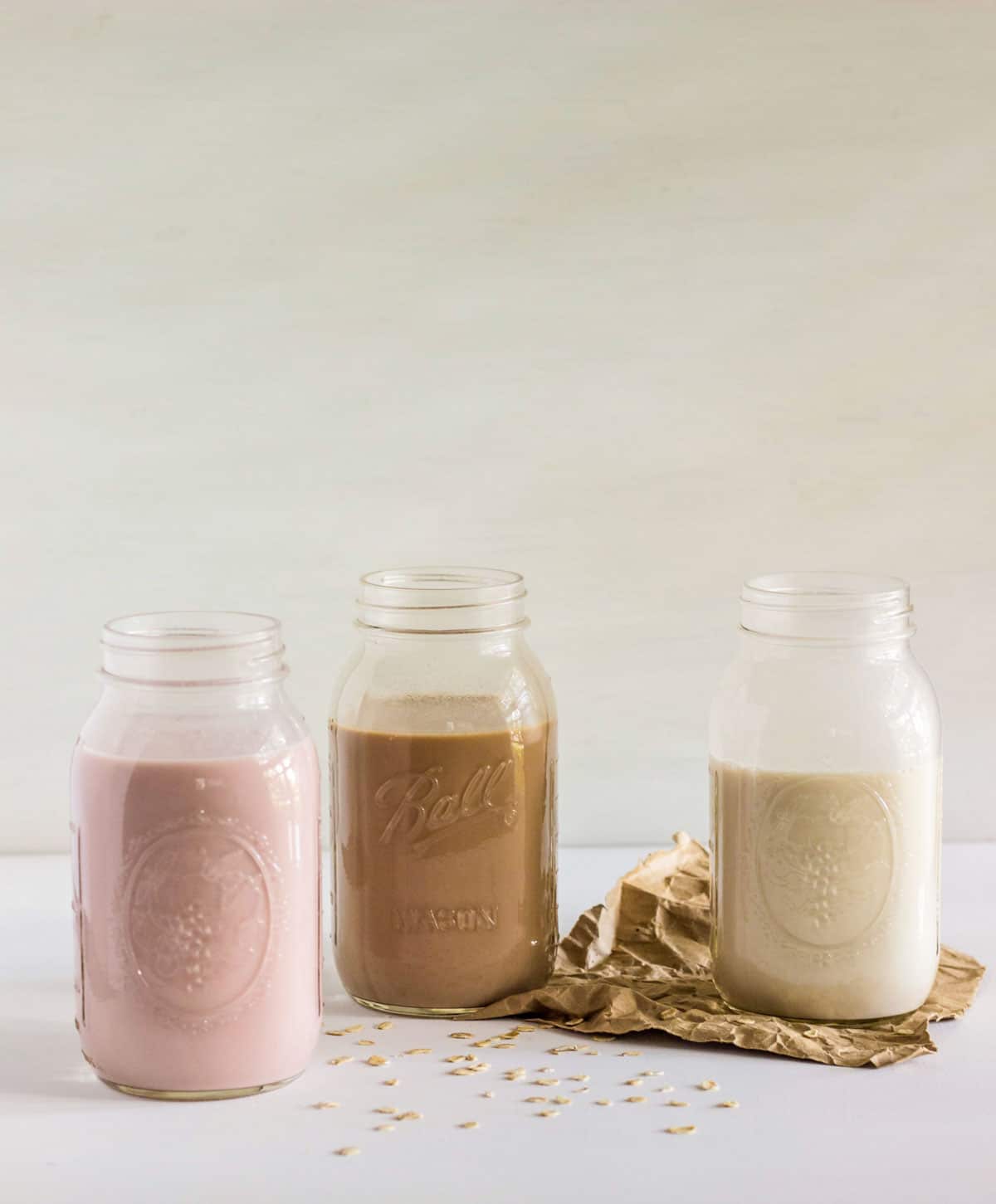 Three jars of different flavored oat milk. Strawberry flavor on the left, chocolate in the middle  and vanilla on the right. 