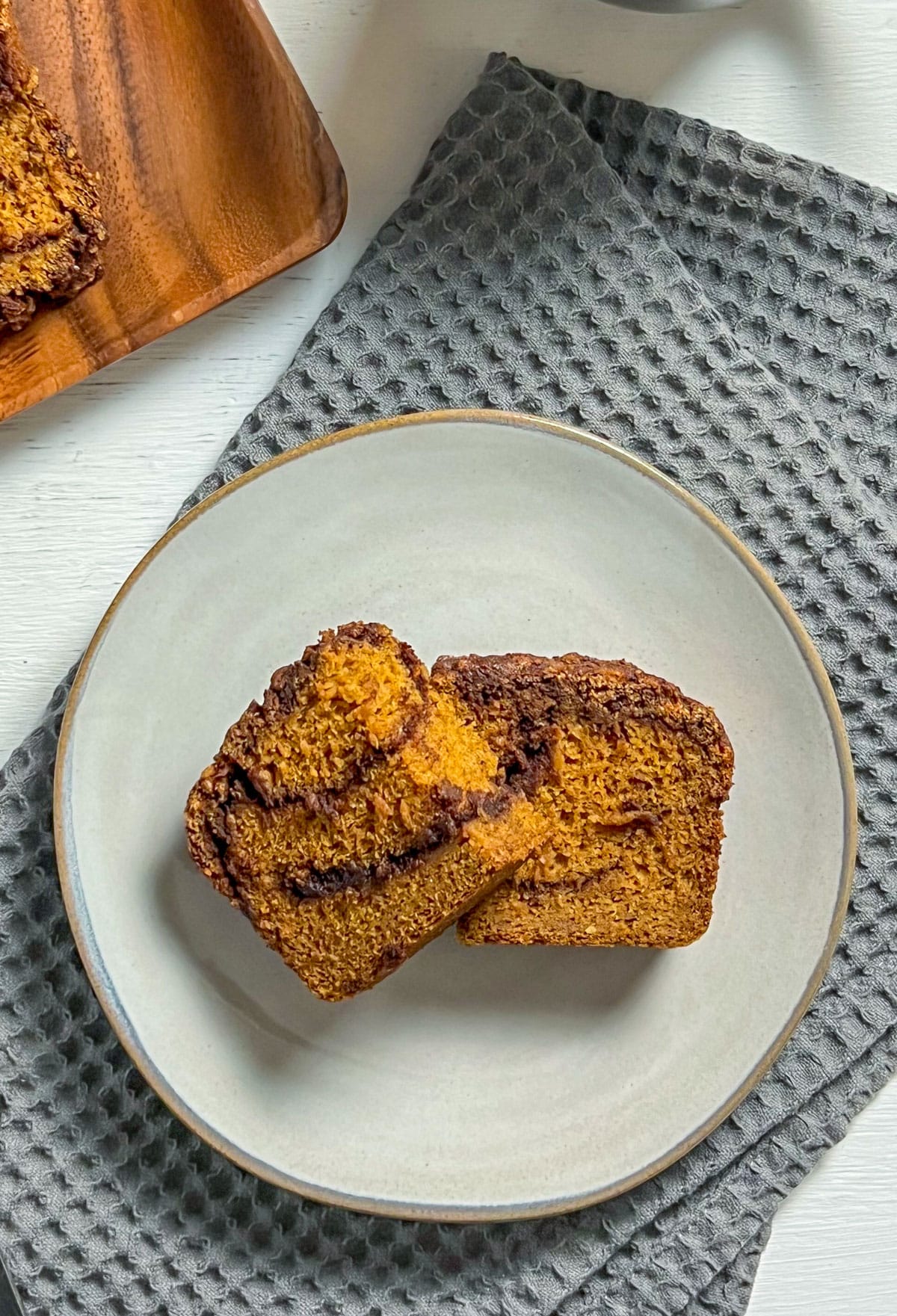 Overhead view of a slice of Pumpkin Cinnamon Swirl Quick Bread on a small plate. The plate sits on a grey textured kitchen towel.