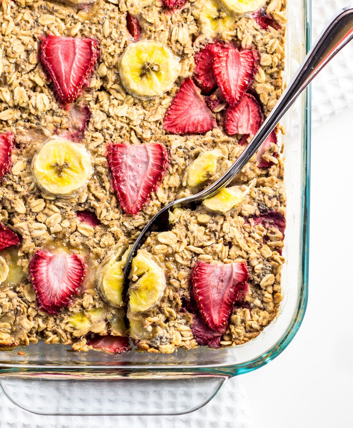 Overhead view of Strawberry Banana Baked Oatmeal in a baking dish. There is a spoon resting in the oatmeal.