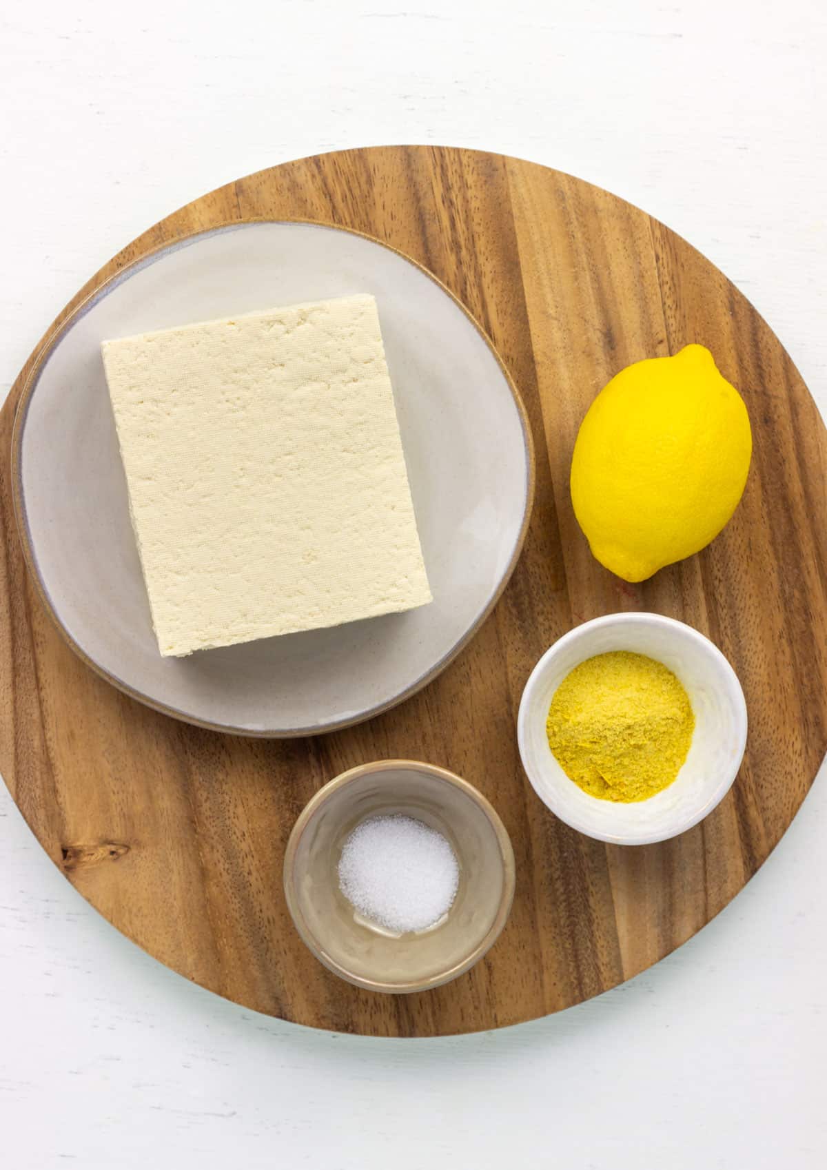 Overhead view of ingredients to make Tofu Cream Cheese. There is a block of tofu and bowls of salt, nutritional yeast and lemon juice.