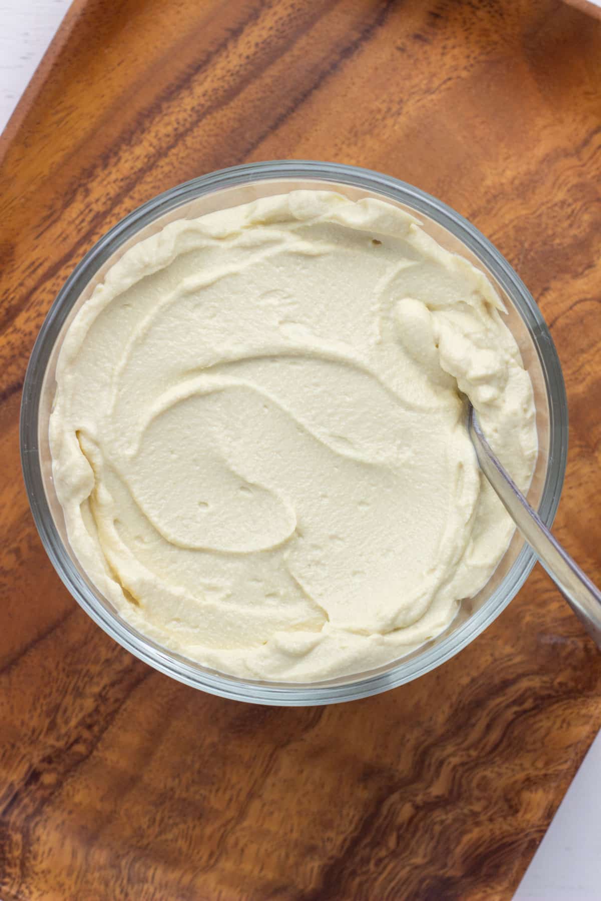 Overhead view of a glass bowl of Tofu Cream Cheese. The bowl is on a wooden tray.