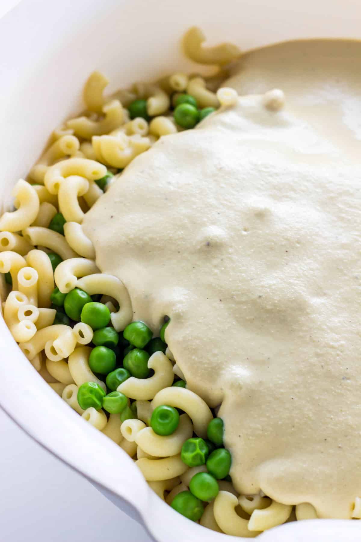 Close up of a bowl of elbow pasta and peas with cashew cheese poured over the top.