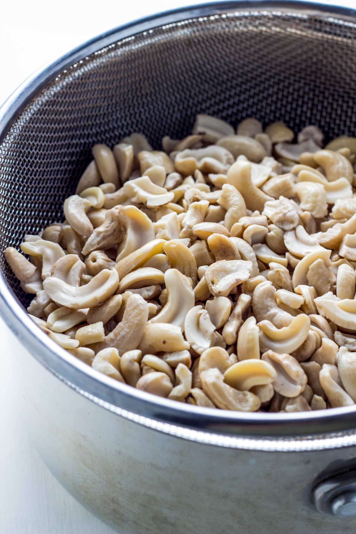 Raw cashews in a strainer over a pot.