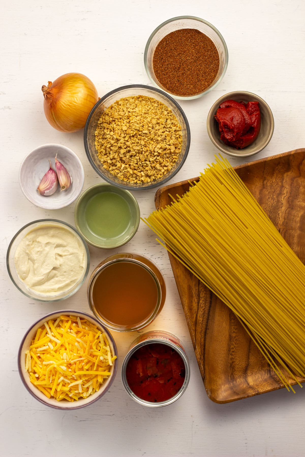 Ingredients to make Vegan Taco Spaghetti. There is uncooked spaghetti, TVP, taco seasoning, tomato paste, onion, garlic, oil, tofu cream cheese, vegetable broth, vegan cheese and diced tomatoes.