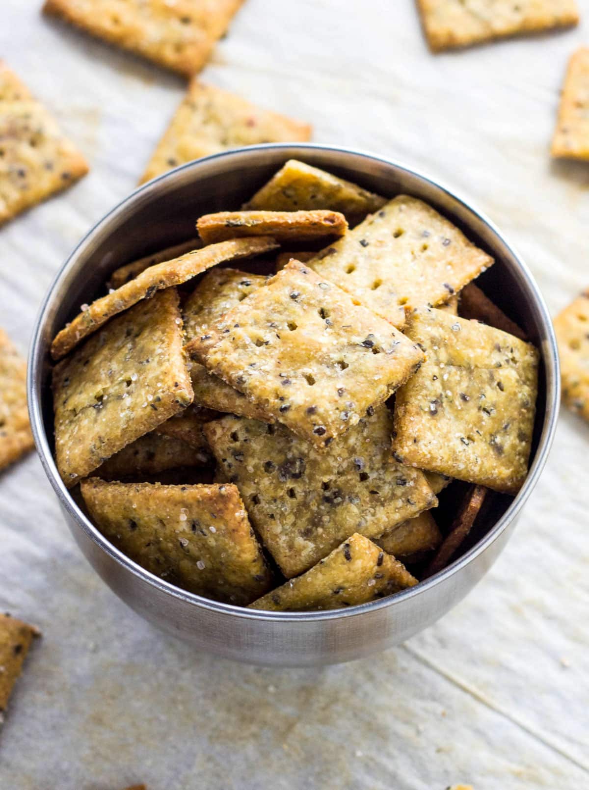 A small metal bowl of Whole Wheat Cheesy Herb Chia Crackers.