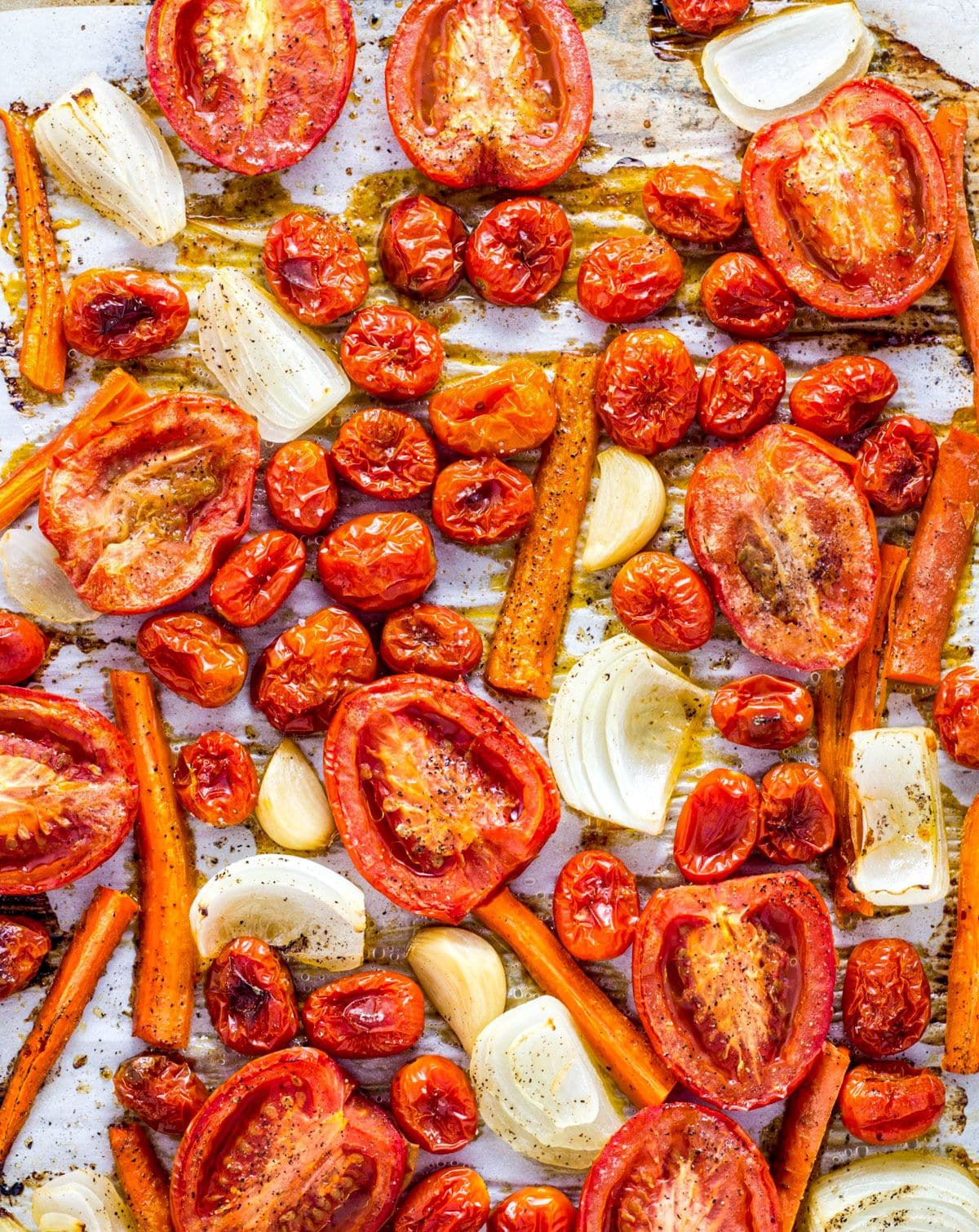 Baked tomato halves, grape tomatoes, onions and carrots with oil, salt and pepper on a baking sheet.
