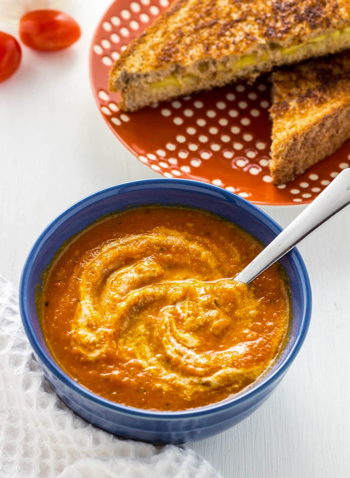 Creamy Roasted Tomato Soup in a small blue bowl. There is a grilled sandwich in the background.