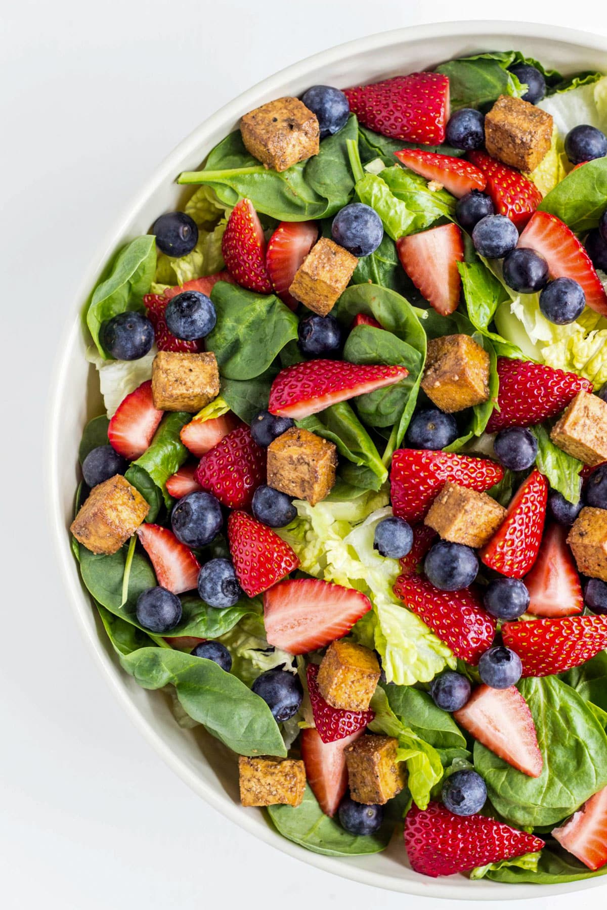 Close up of a salad with spinach, strawberries, blueberries and balsamic tofu cubes.