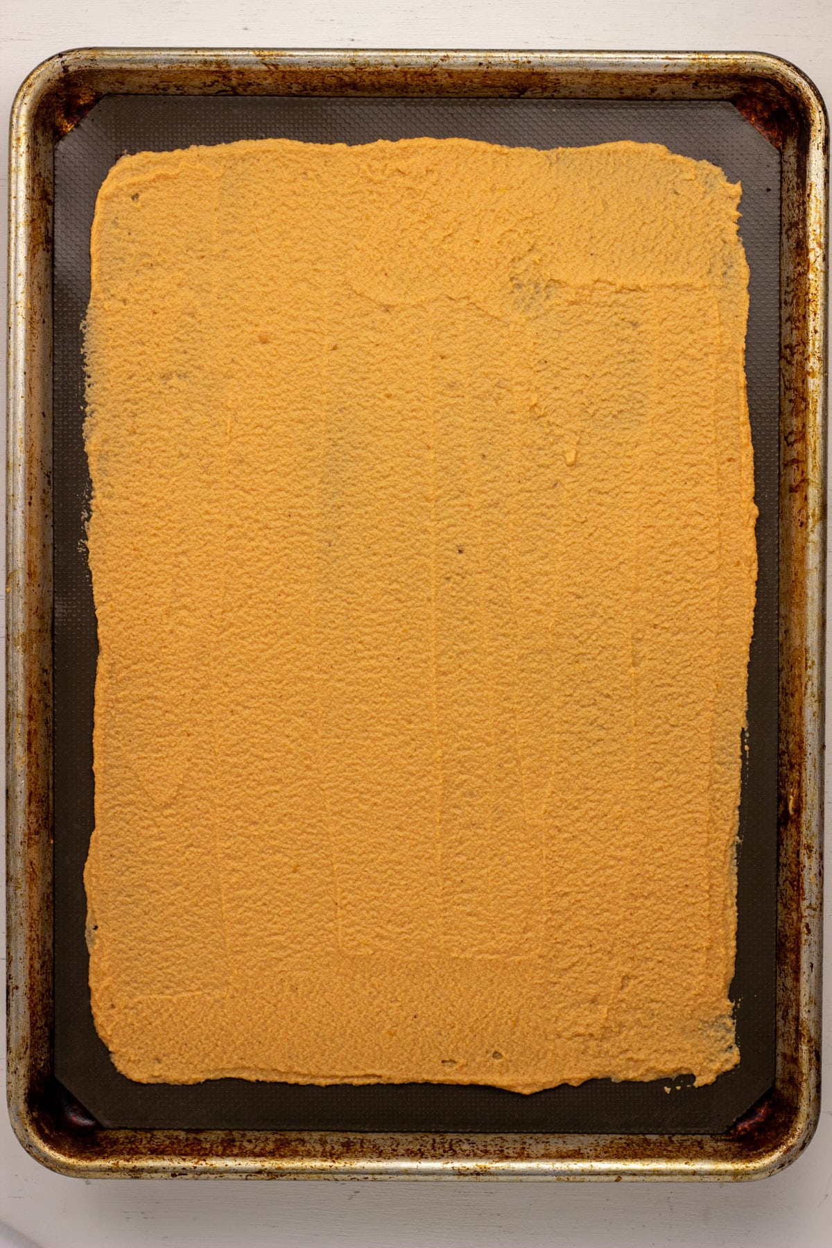 Overhead view of a sheet pan with cracker batter spread in a rectangle on parchment paper.