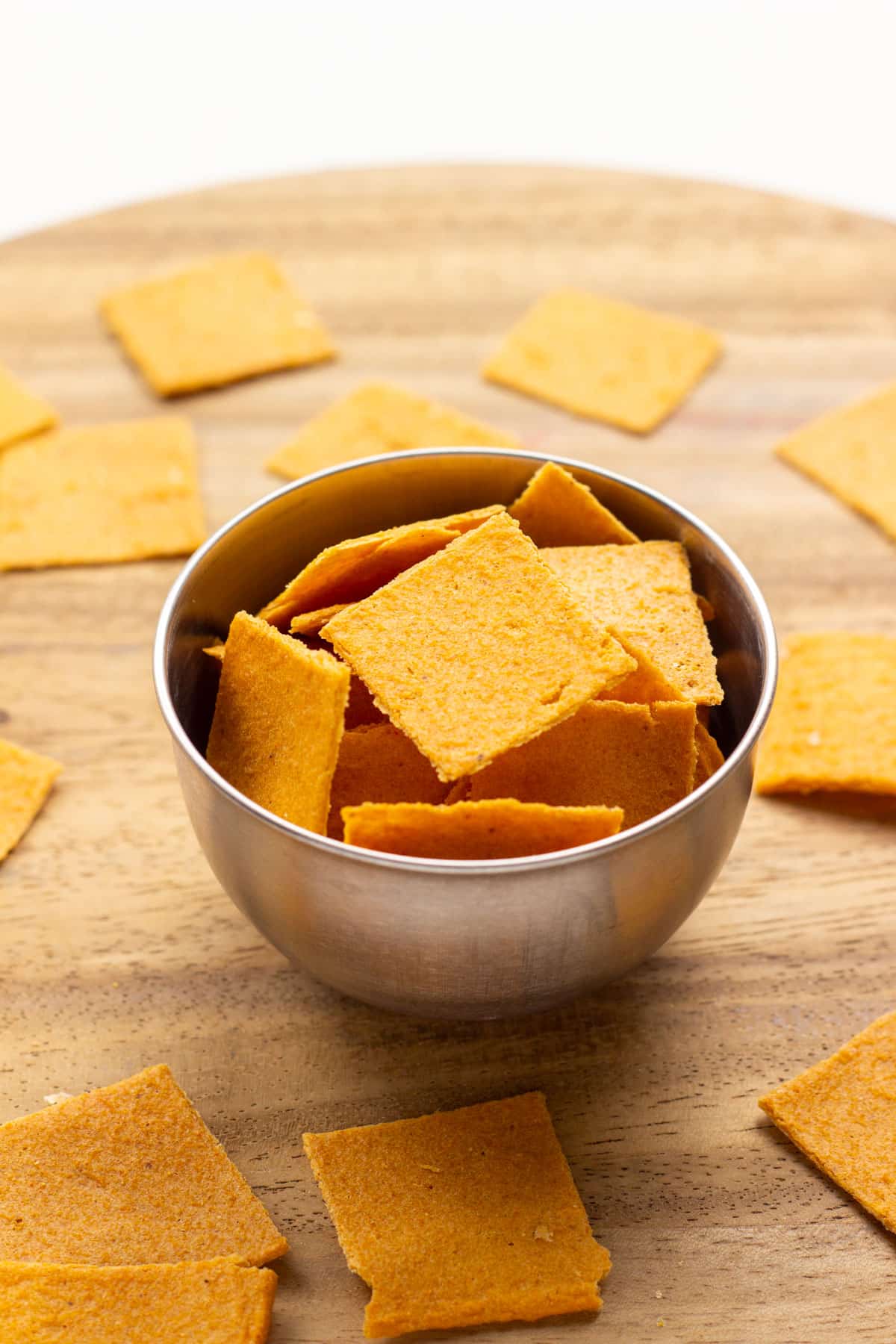 Smoky Red Lentil Crackers in a small metal bowl. The bowl is sitting on a wooden board. There are also crackers around the bowl.