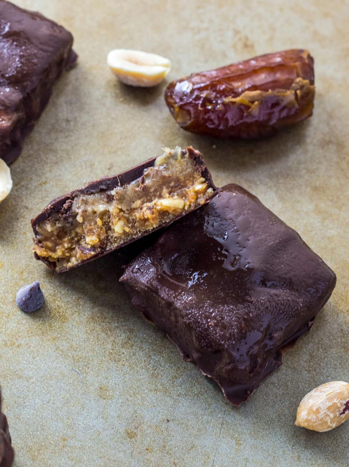 Close up view of the inside of a Vegan Peanut Butter Snickers Bite. There are dates and roasted peanuts in the background.