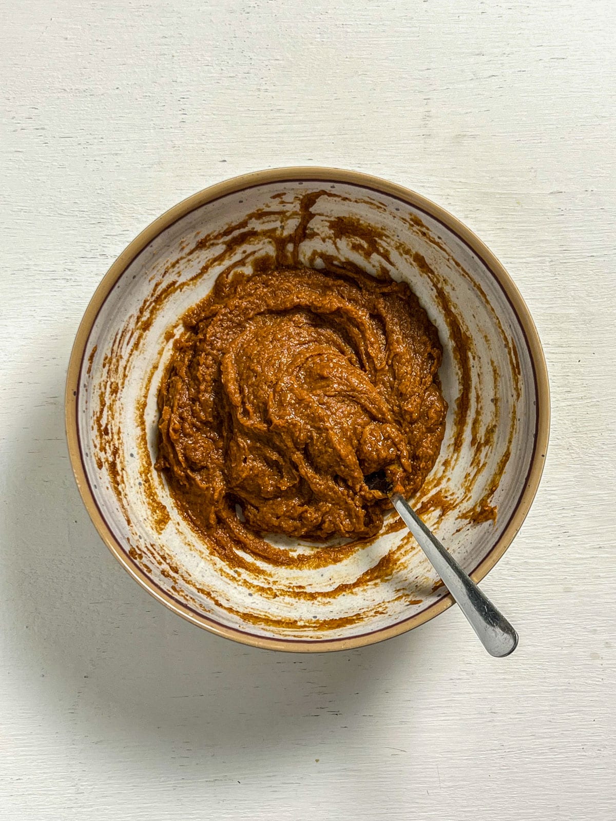 Overhead view of a bowl of pumpkin peanut butter filling. There is a spoon resting in the bowl.