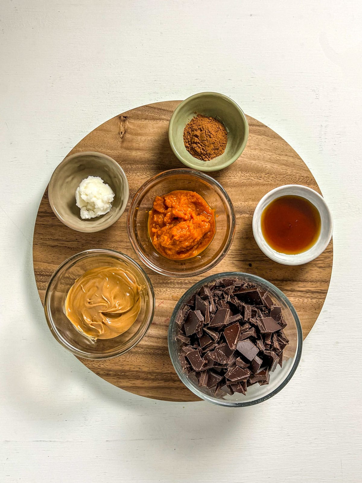 Ingredients to make Vegan Pumpkin Peanut Butter Cups. There are bowls of chopped chocolate, peanut butter, maple syrup, pumpkin puree, coconut oil and pumpkin pie spice.