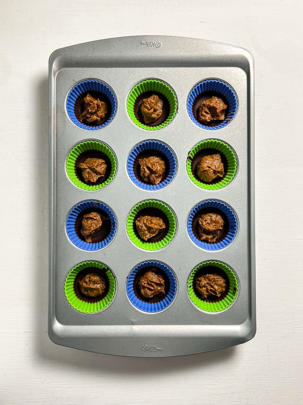 Overhead view of a muffin pan with a layer of chocolate in the bottom topped with pumpkin peanut butter filling.