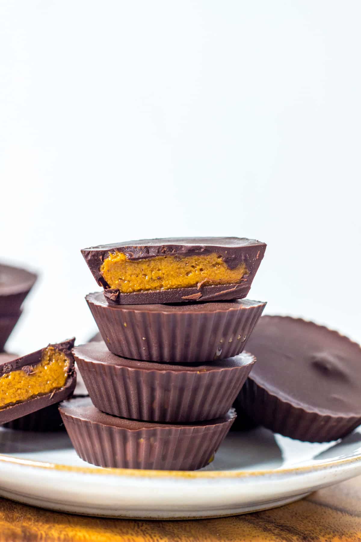 A stack of Vegan Pumpkin Peanut Butter Cups. The top cup is cut in half to show the inside.
