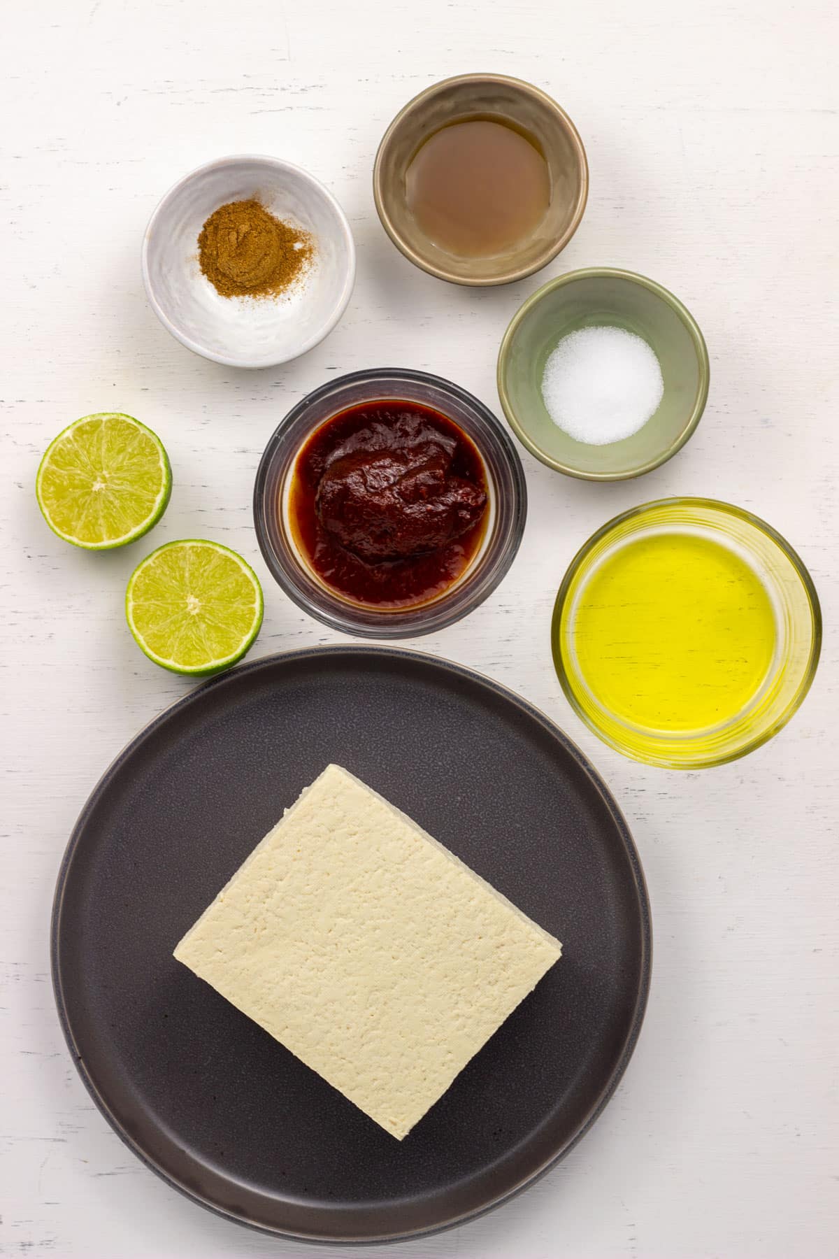 Ingredients to make Chipotle Pepper Marinated Tofu. There is a block of extra firm tofu, olive oil, chipotle pepper in adobo sauce, salt, maple syrup, ground cumin and limes.