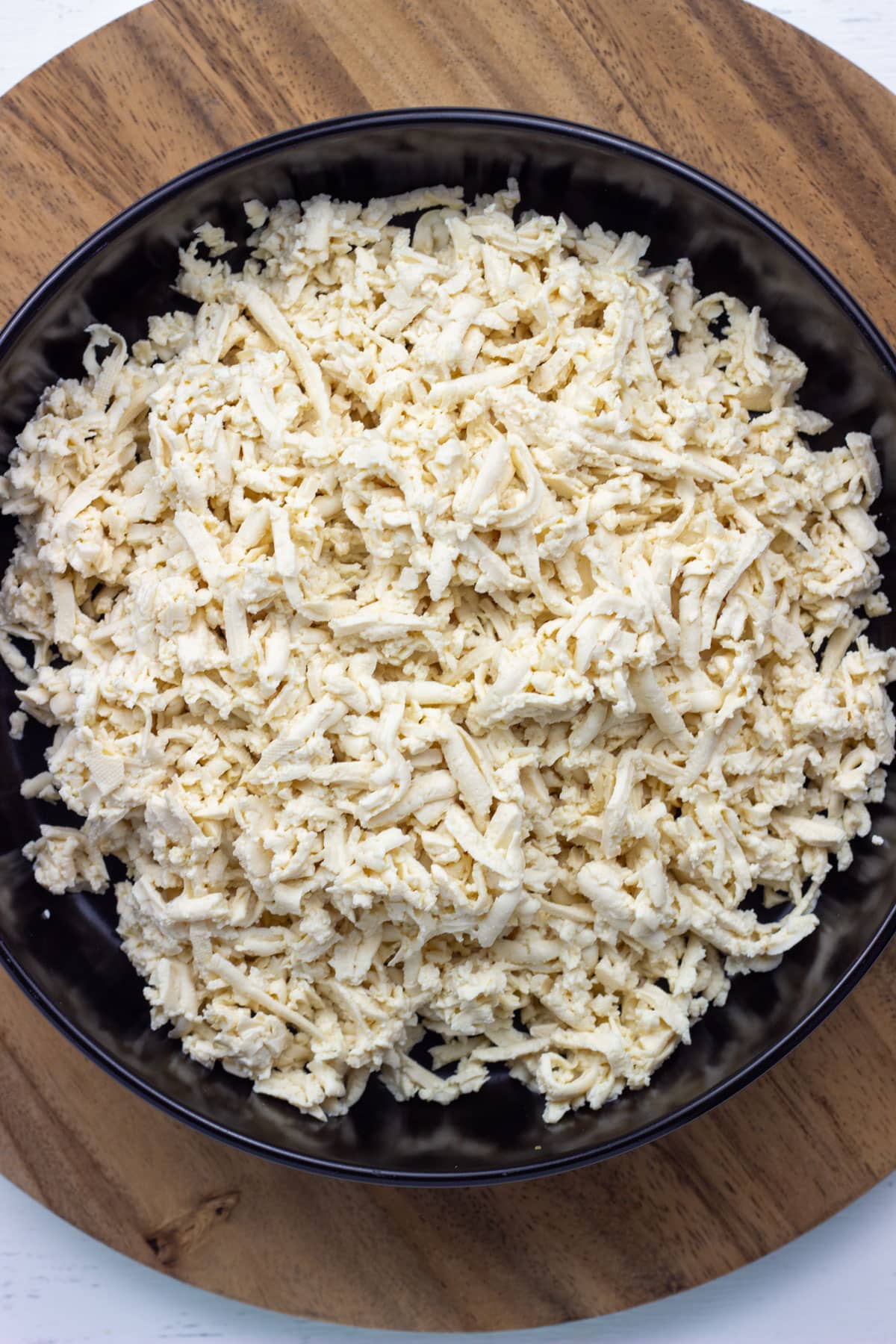 A bowl of shredded tofu sitting on a wooden board.