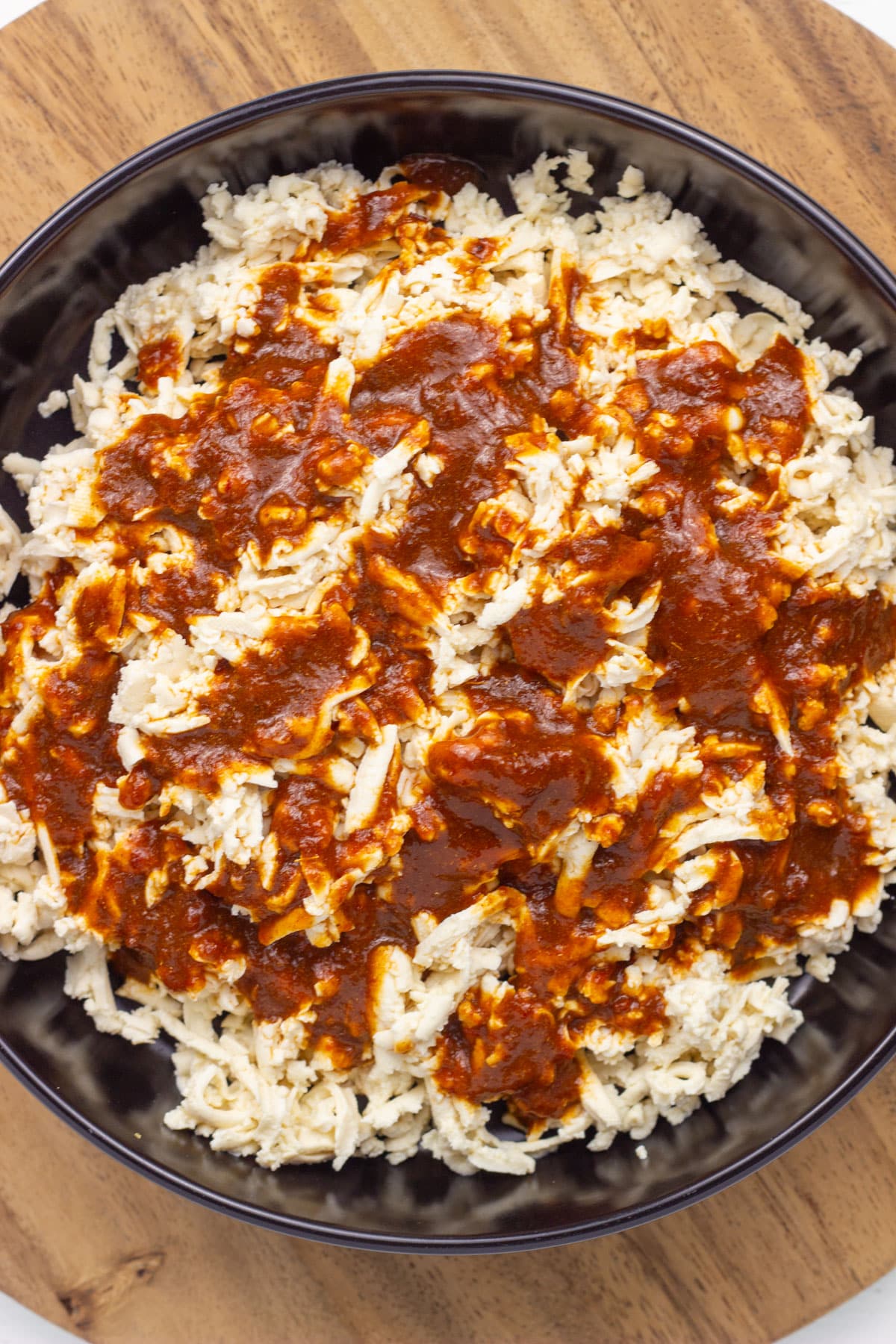 An overhead view of a bowl of shredded tofu with chipotle sauce poured over it.