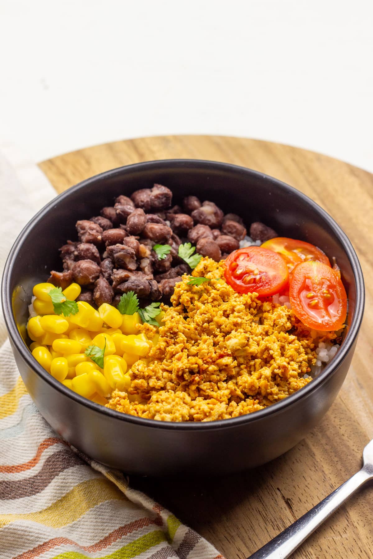 A bowl with Chipotle Pepper Marinated Tofu, corn, black beans, tomatoes and cilantro lime rice.